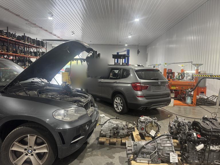 Two BMW SUVs being dismantled, with transmissions and engines on pallets